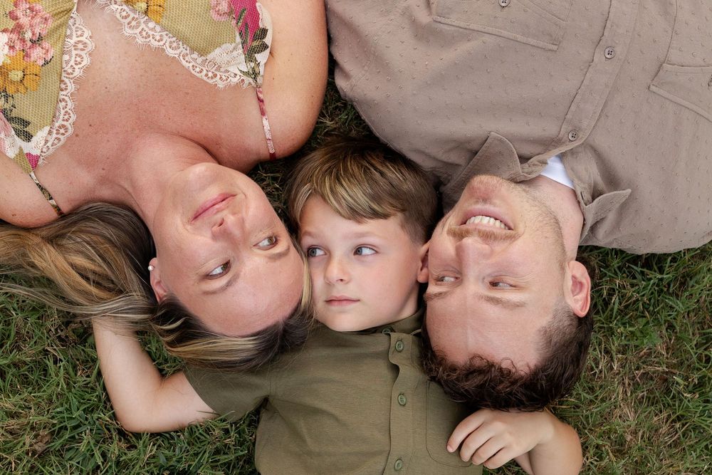 Smiling woman, boy and man lying on green grass with their heads together, viewed from above in a happy family portrait.