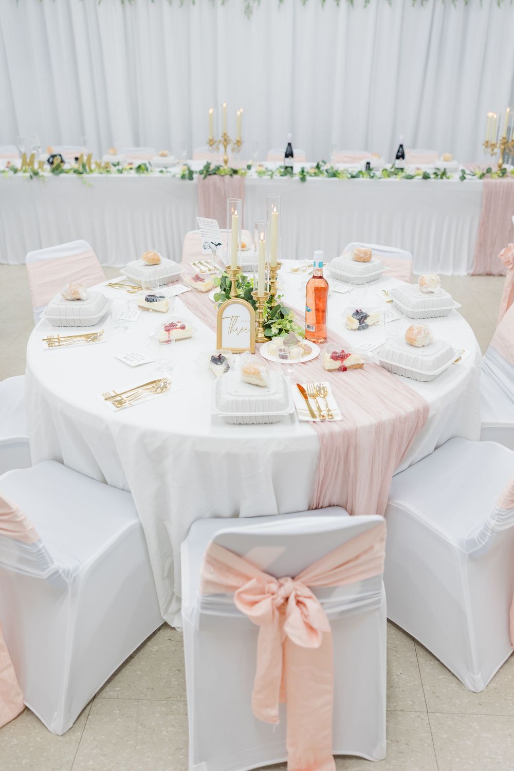 Elegant wedding reception table with white linens, pink bow chair covers, gold candles, and blush runner centerpiece.