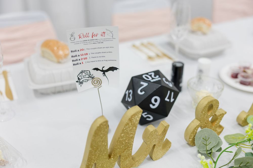 Dungeons & Dragons themed wedding table with black D20 dice, gold letter decor, and a roll for it sign.