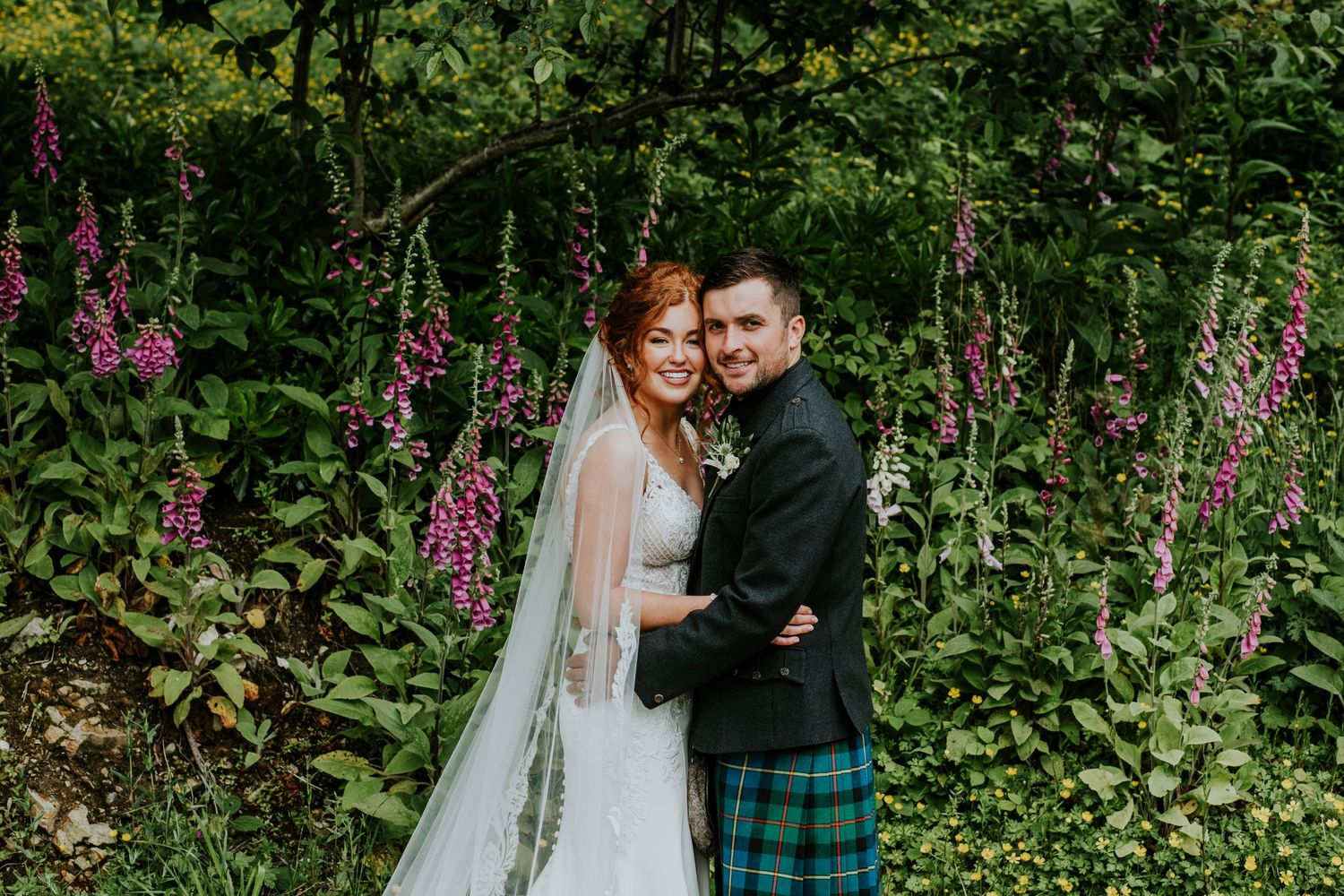 Wedding couple embracing among purple foxgloves and lush garden greenery.