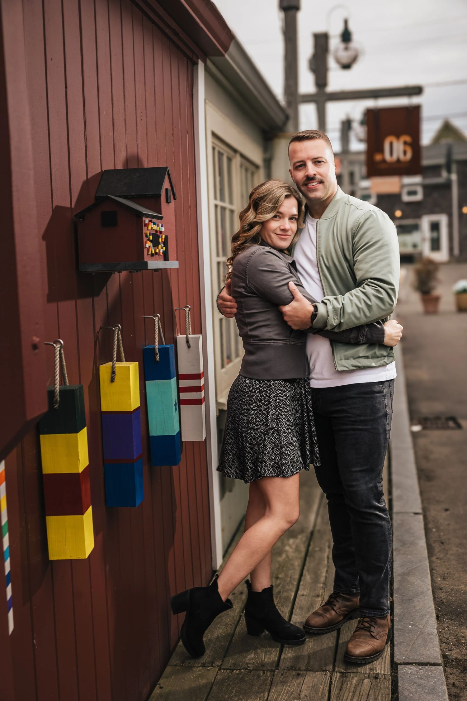 Couple posing together outside a red barn, embracing while standing by the entrance. Engagement at Rockport Harbor, Rockport, MA