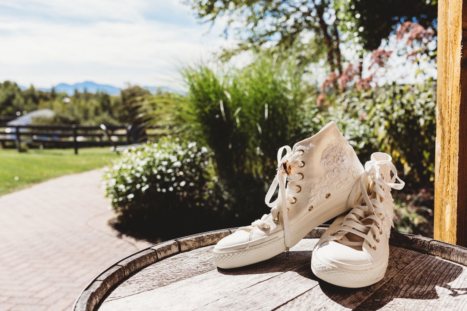 Lace high-top bridal sneakers displayed on a wooden barrel overlooking the wedding grounds.