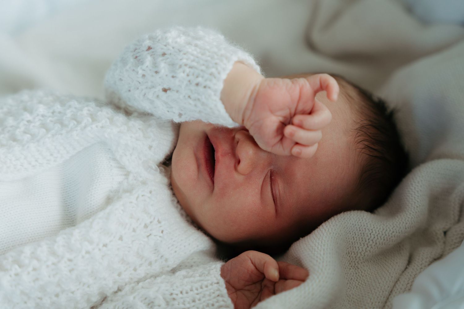 Tattooed adult hands gently cradling tiny newborn baby feet wrapped in a soft green blanket.