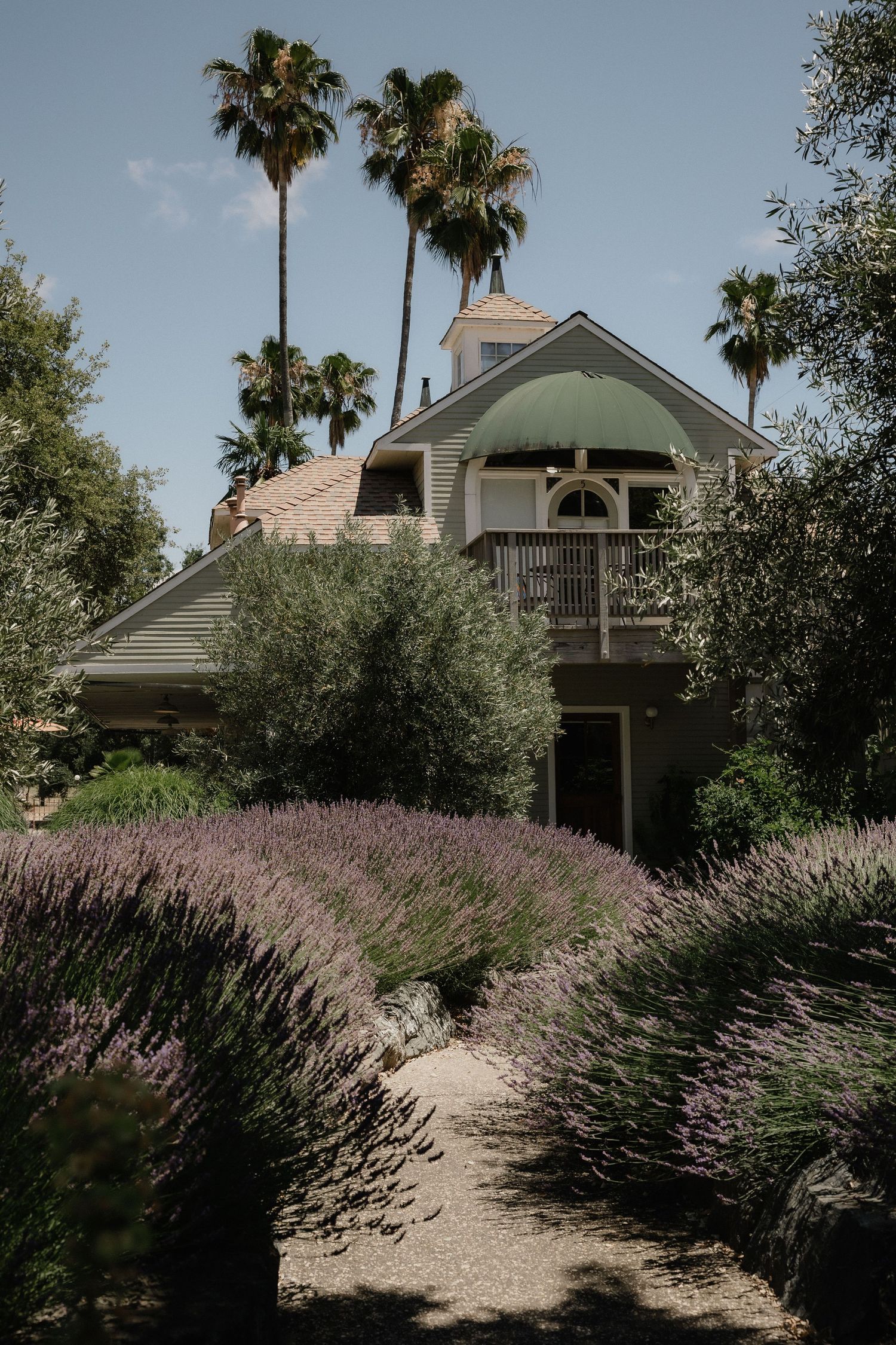 Charming wedding venue with lavender gardens, lush greenery, and palm trees framing a two-story building with a green dome.
