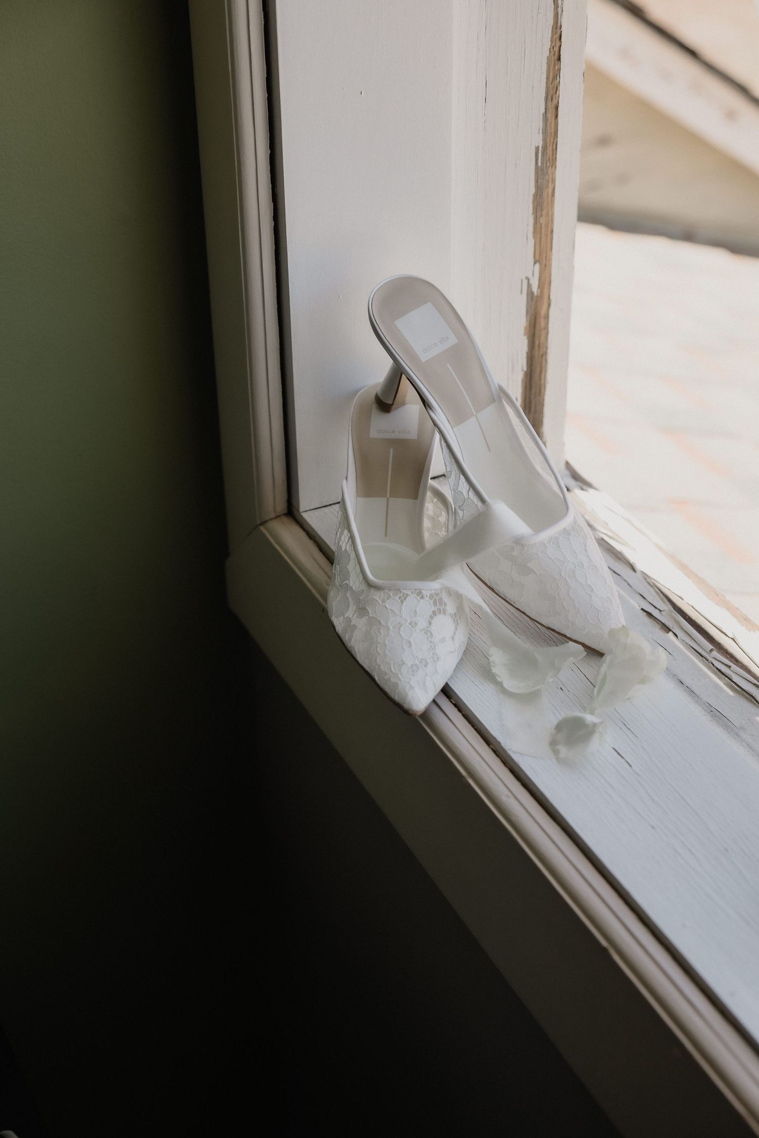 White lace bridal heels resting on a window sill with soft natural light.