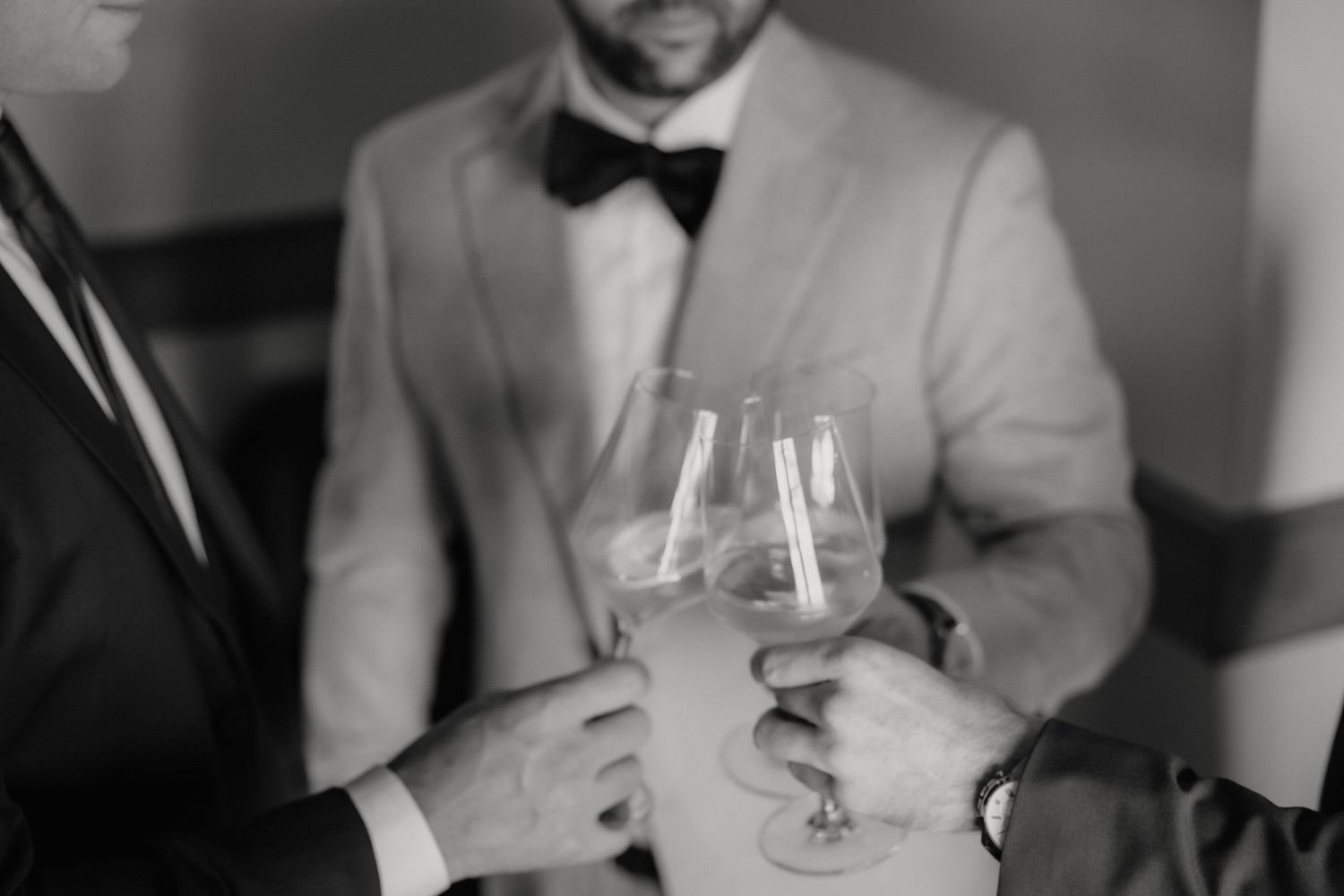 Black and white photo of two men in formal suits clinking wine glasses at an elegant event or wedding celebration.
