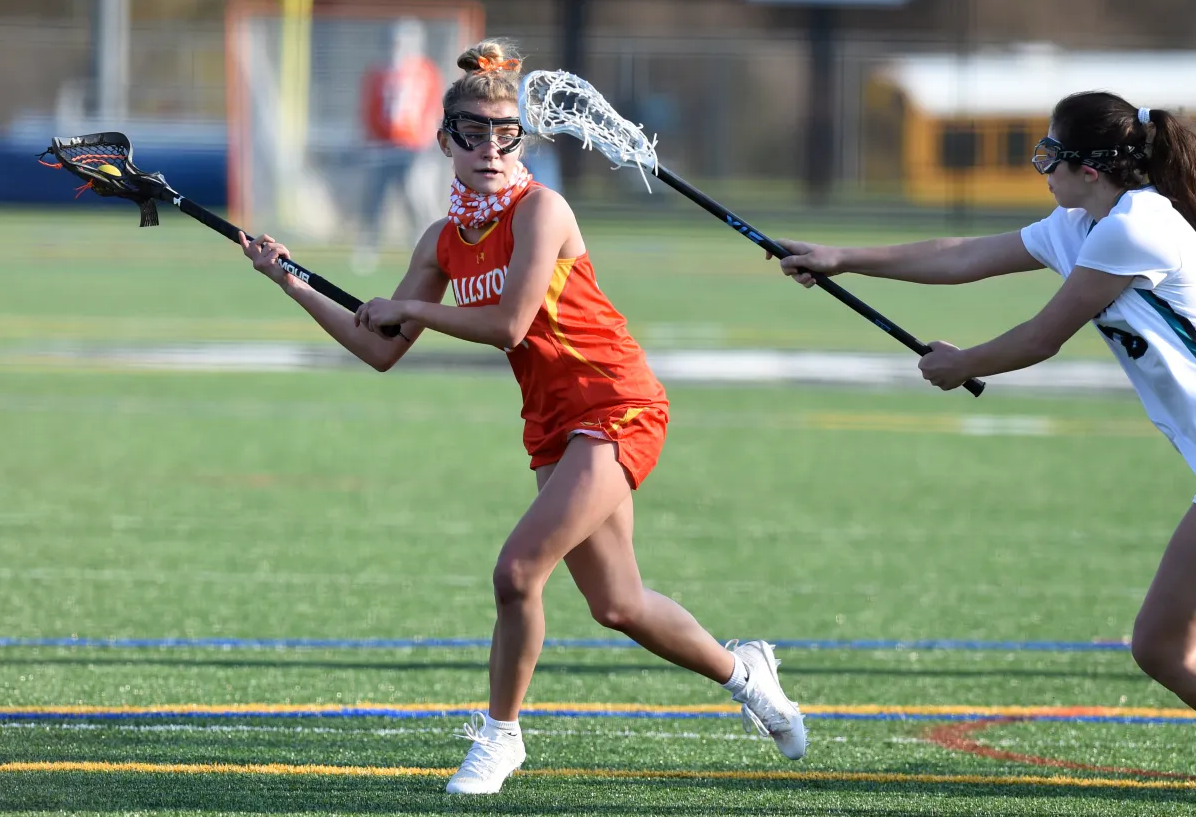 Close-up of lacrosse sticks held up against a golden sunset sky outdoors.