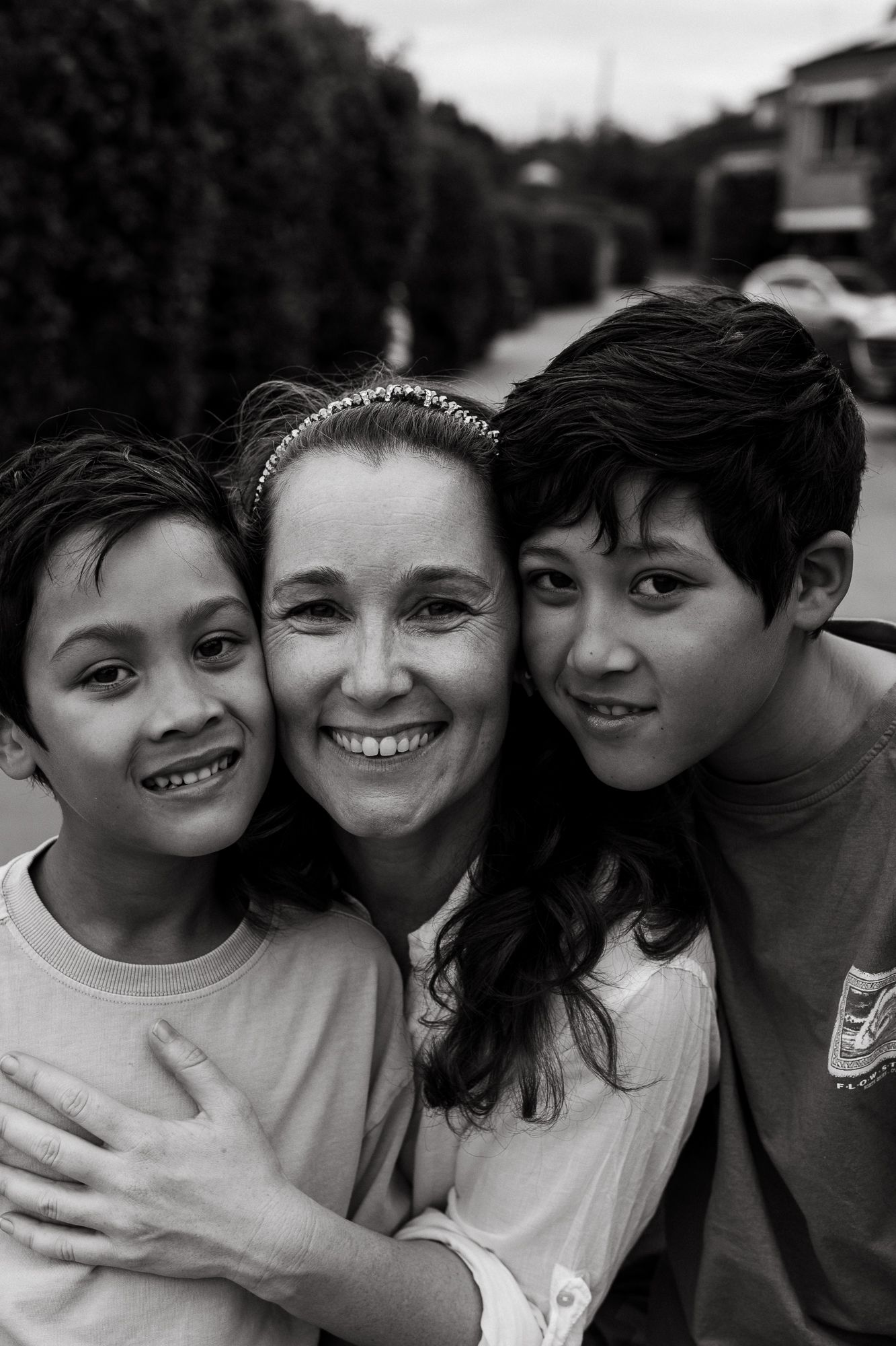 Black and white portrait of a smiling woman with two boys hugging outdoors.