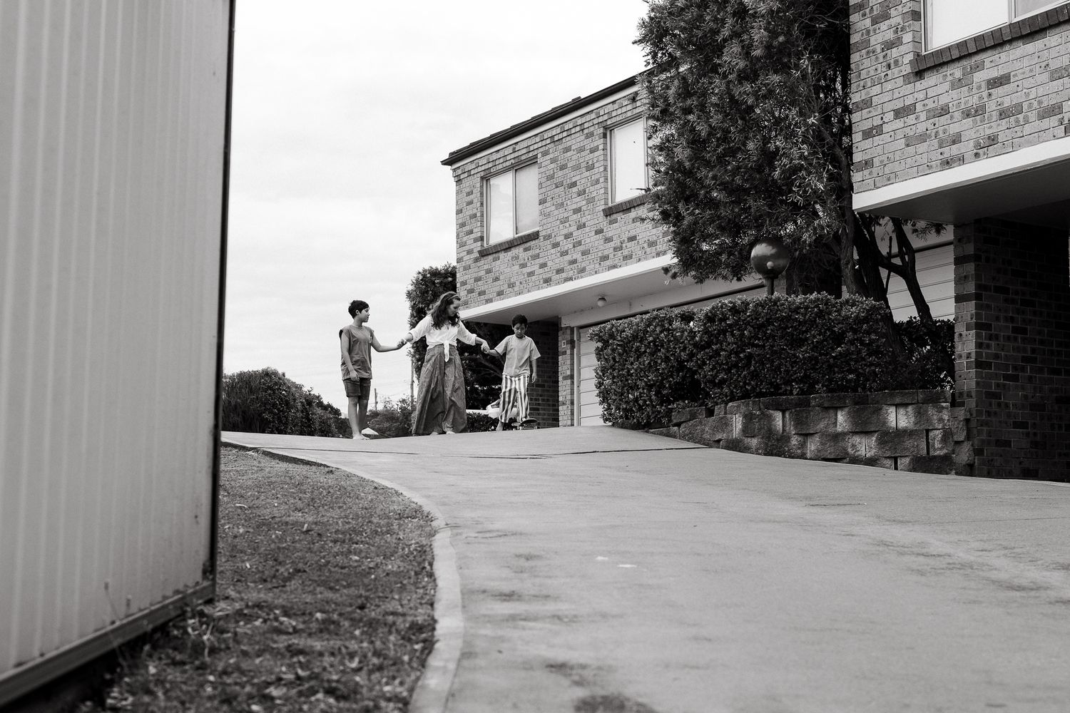 Black and white photo of people gathered on a suburban driveway beside a brick house.