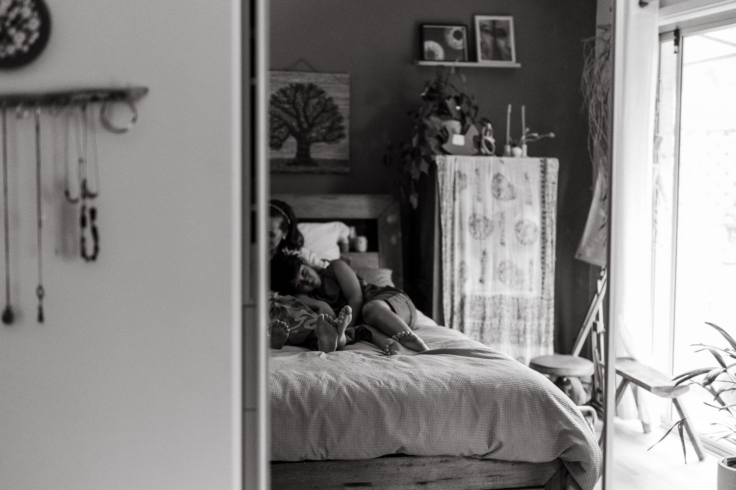 Black and white photo of a person resting on a bed in a cozy bedroom with vintage decor and natural light.