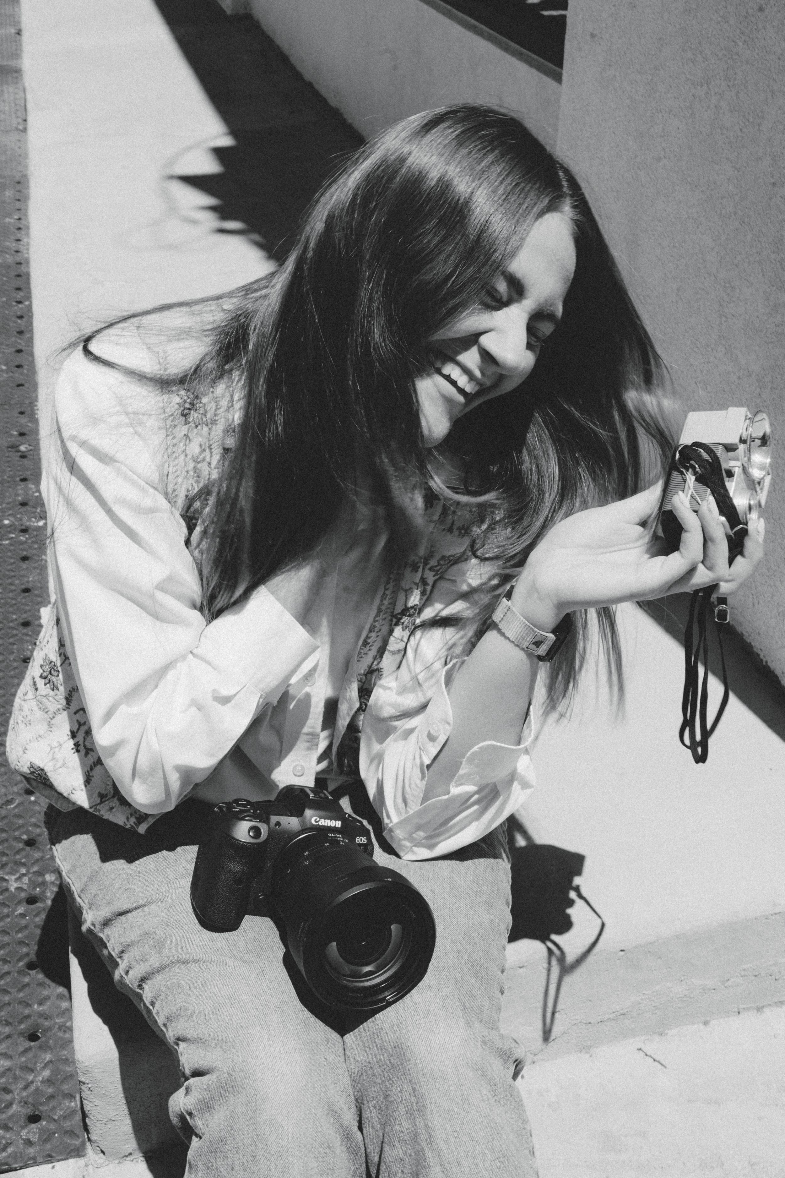 Smiling young woman with long brown hair wearing a white shirt and embroidered vest, posing against a colorful striped wall.