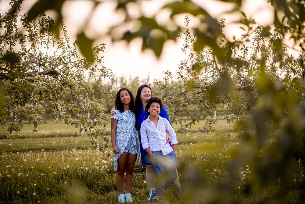 A group poses together in a blooming spring orchard at sunset with bokeh light effects in the background.