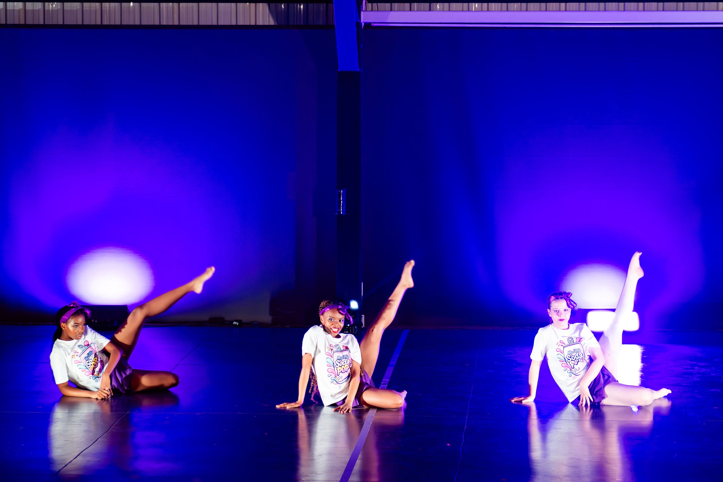 Young dancers performing a lively routine under colourful stage lighting.