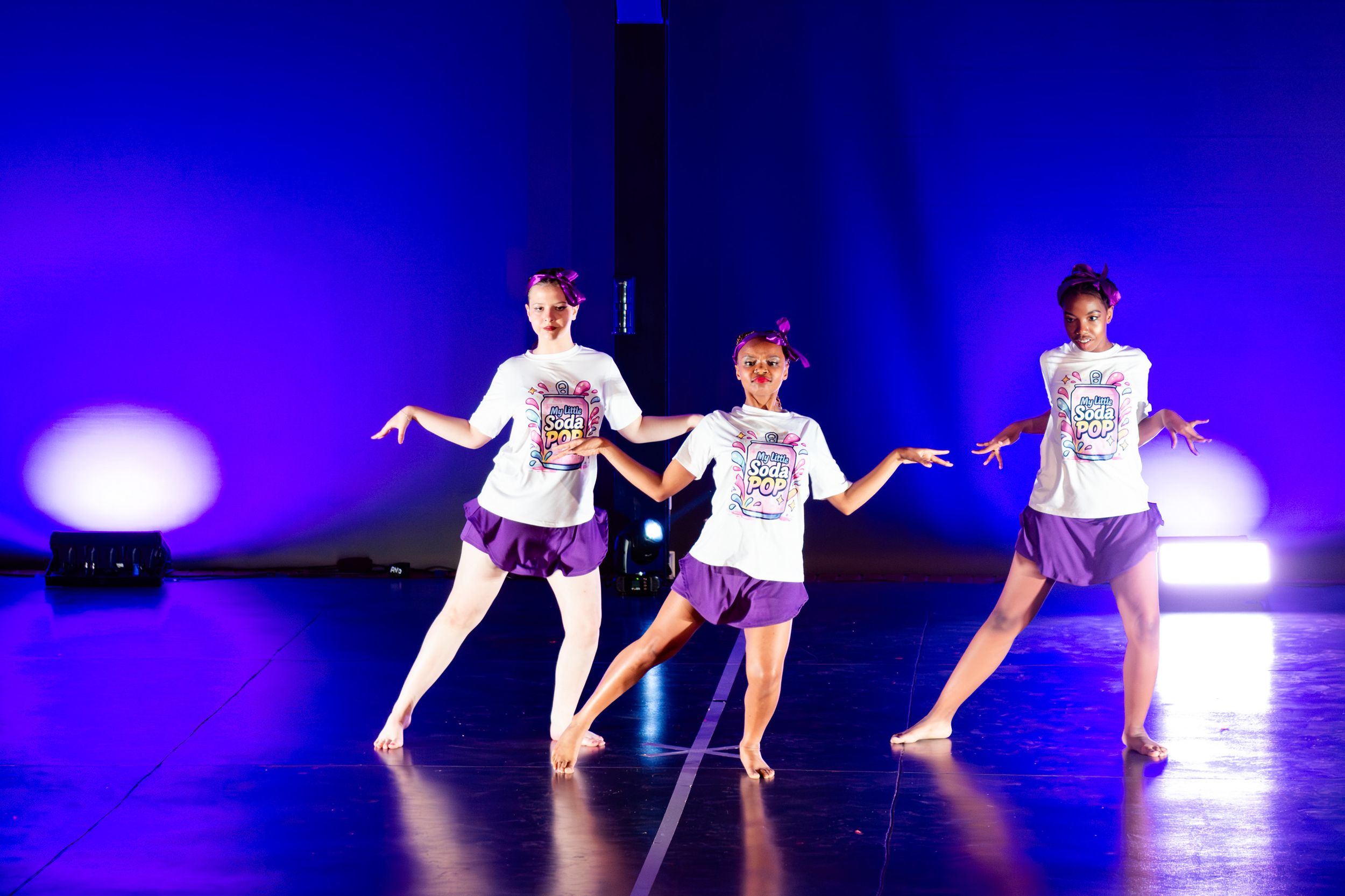 Young dancers performing a contemporary routine under blue stage lighting.