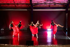 Dancers performing a dramatic choreographed routine under vibrant red stage lighting.