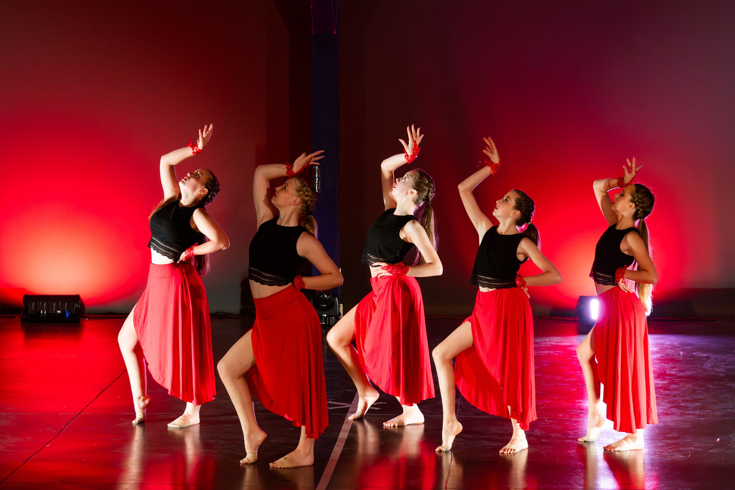 A group dance performance captured under vibrant red stage lighting.