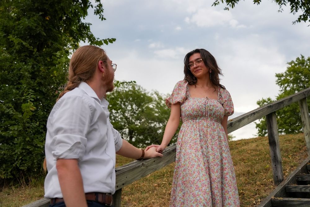 Young couple holding hands on outdoor wooden stairs surrounded by lush green trees.