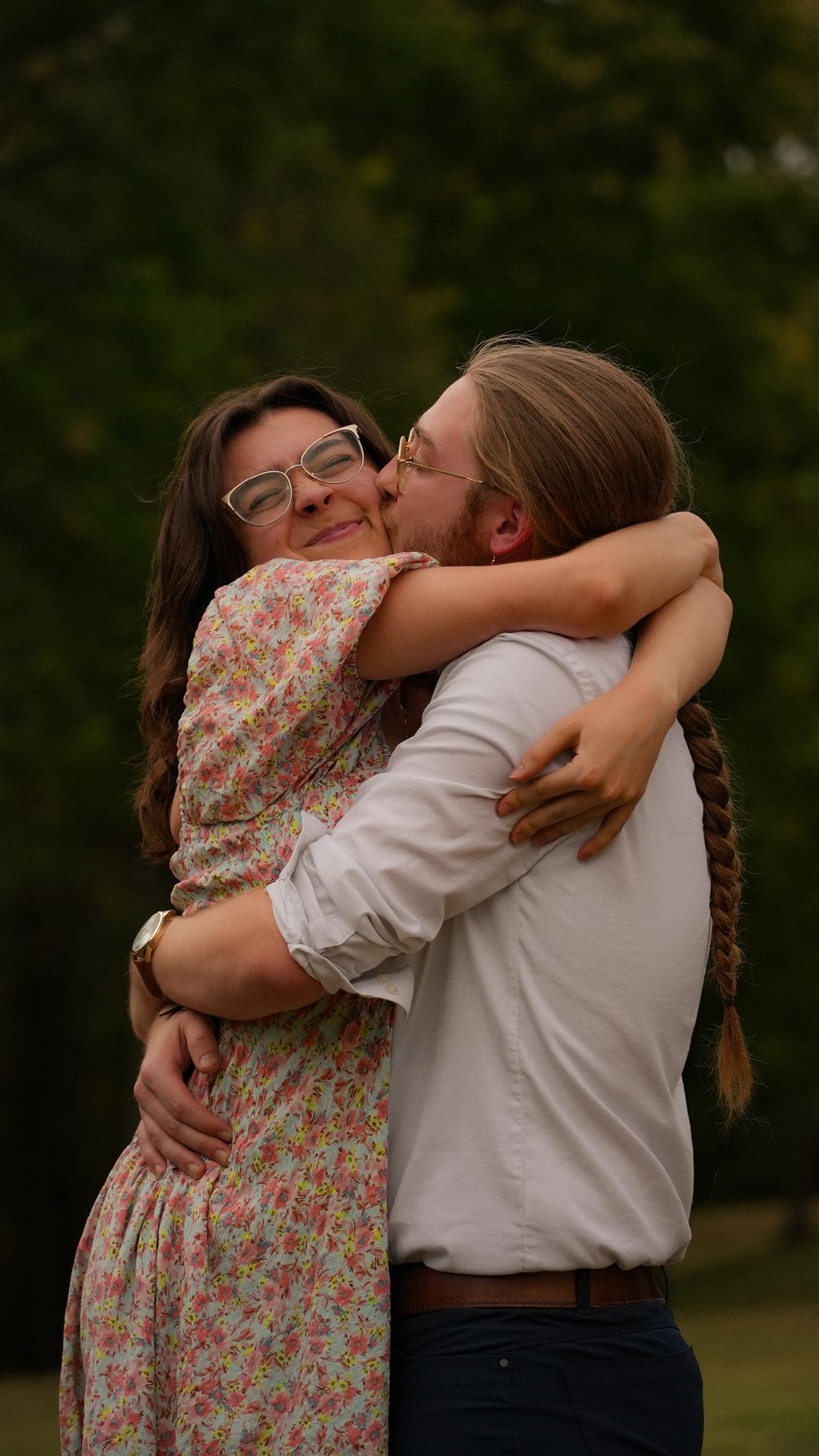Couple sharing a tender kiss and embrace outdoors with a lush green background.
