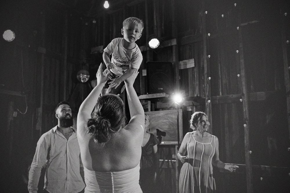 Black and white image of a child held high on the dance floor at a wedding reception.