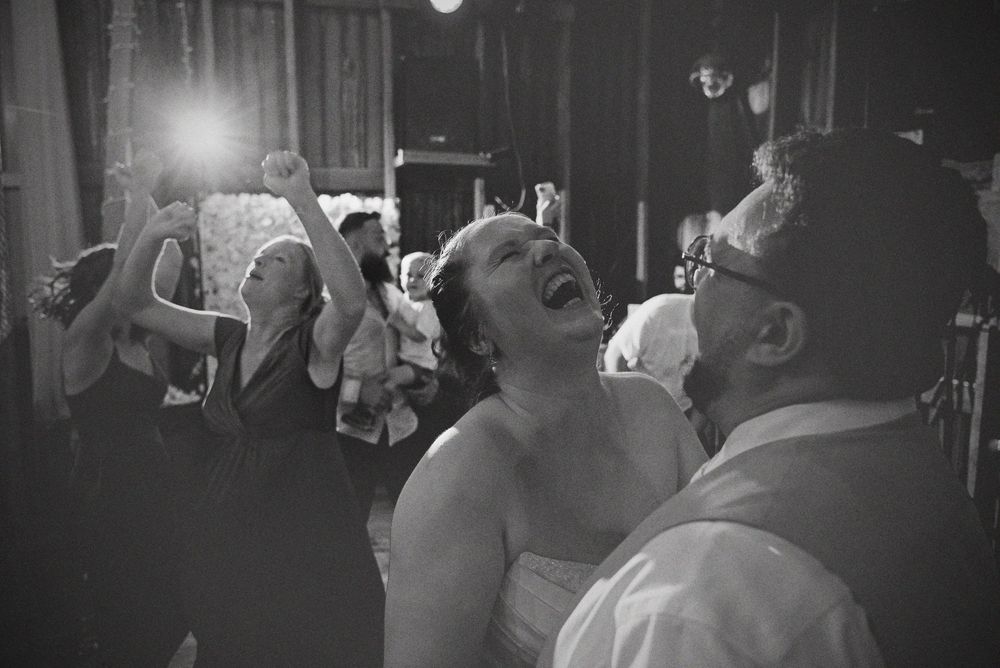 Candid black and white wedding photo of a bride laughing during a high-energy barn dance party celebration.