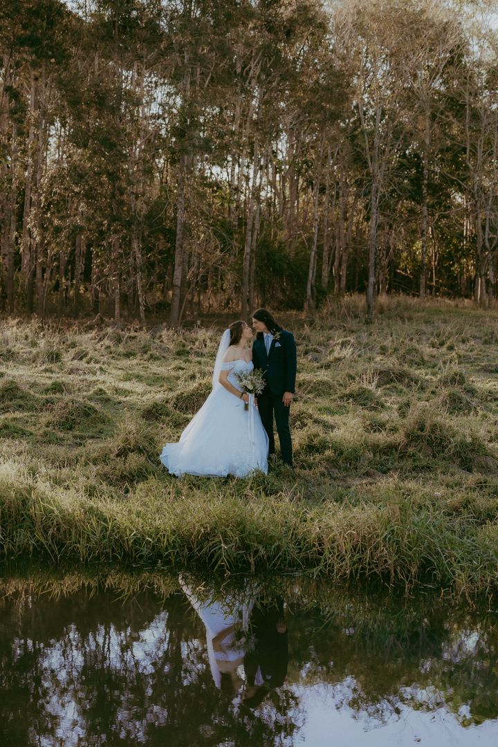 Bride and groom sharing romantic kiss near reflective pond surrounded by paperbark forest.