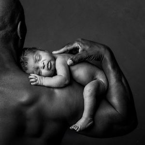 Black and white photo of a sleeping newborn baby cradled in the muscular arm of an adult.