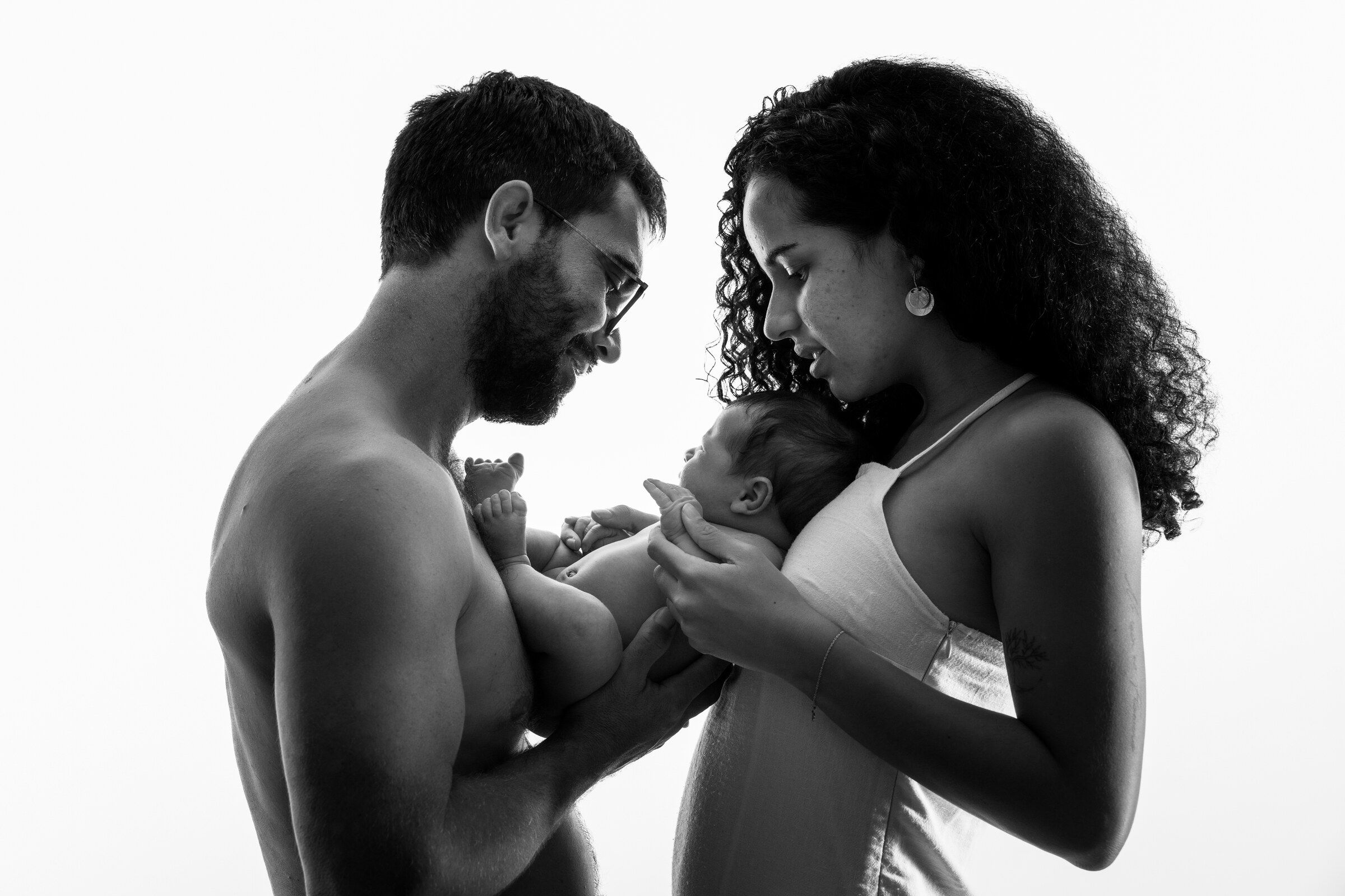 Black and white photo of parents lovingly holding their newborn baby together in a studio setting.