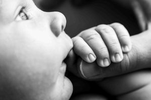 Black and white close-up of a newborn baby grasping an adult finger, symbolizing new life and parental bond.