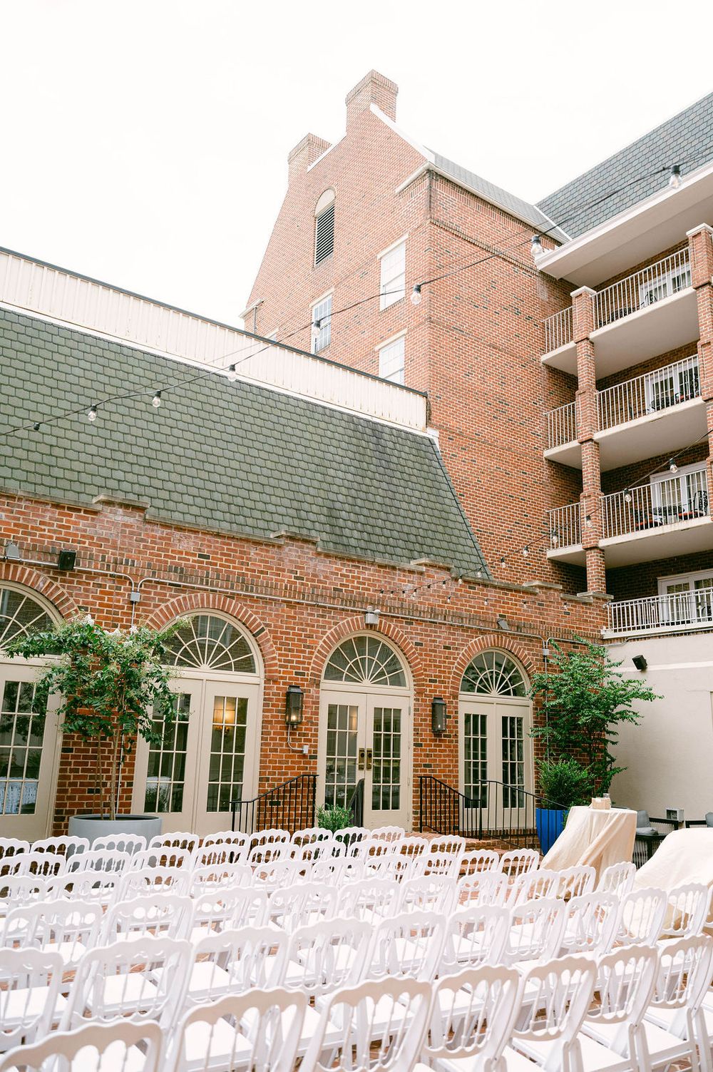 Rows of white chairs arranged in a brick courtyard for an outdoor wedding ceremony at a historic brick building.