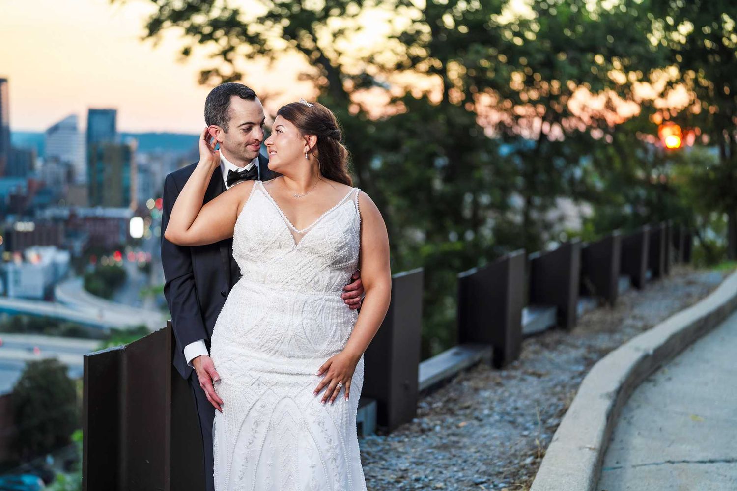 Bride and groom embrace at sunset with city skyline backdrop, at view venue