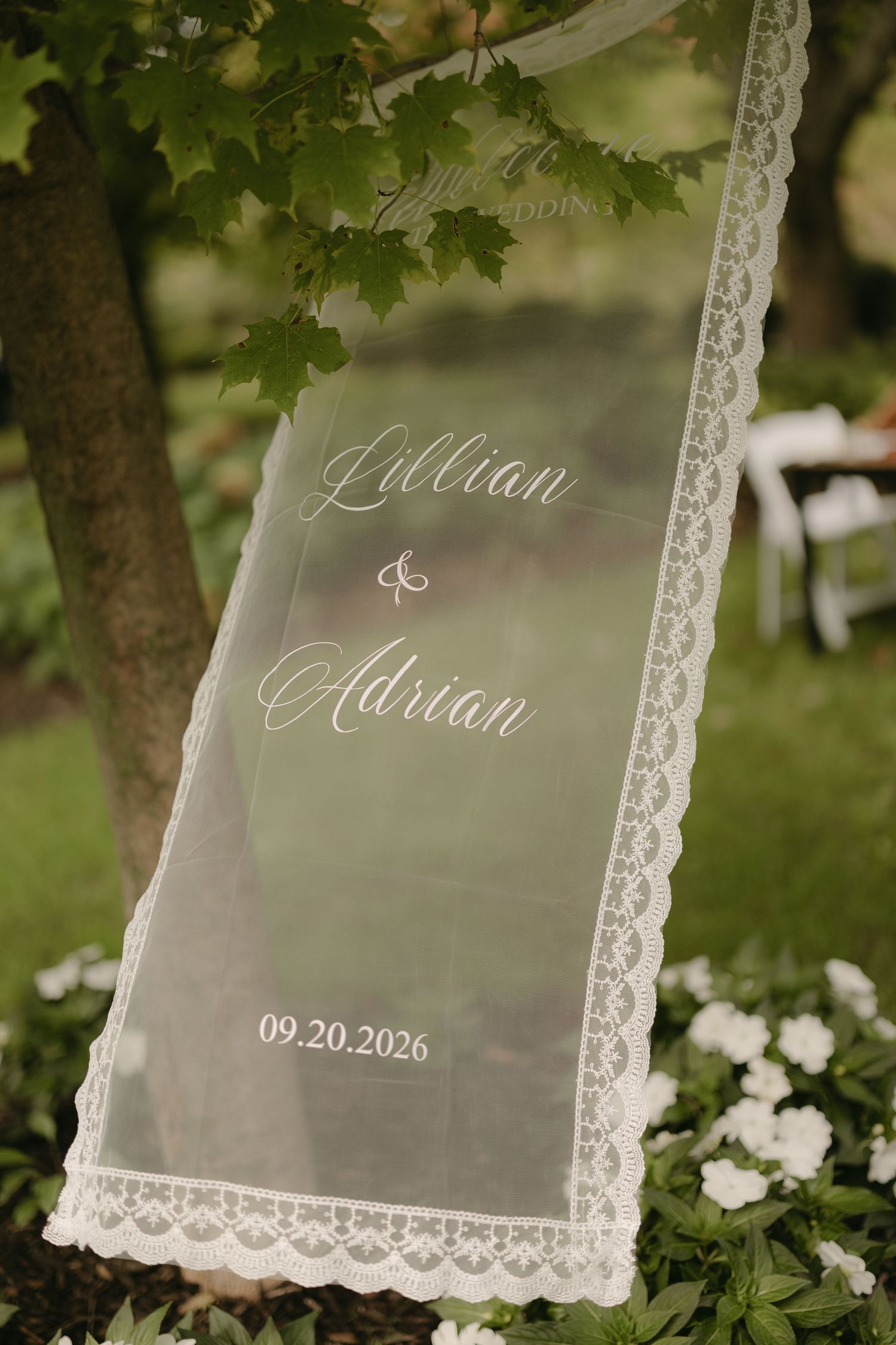Elegant wedding welcome sign on sheer lace fabric reading Lillian and Adrian dated 09.20.2026.