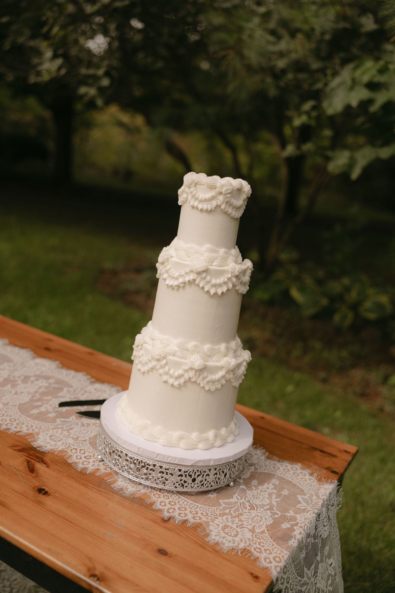 Elegant three-tier white wedding cake with ruffled fondant details displayed on a lace-covered wooden table.