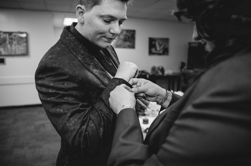 Black and white photo of a groom having his boutonniere pinned on his jacket lapel before the wedding ceremony.