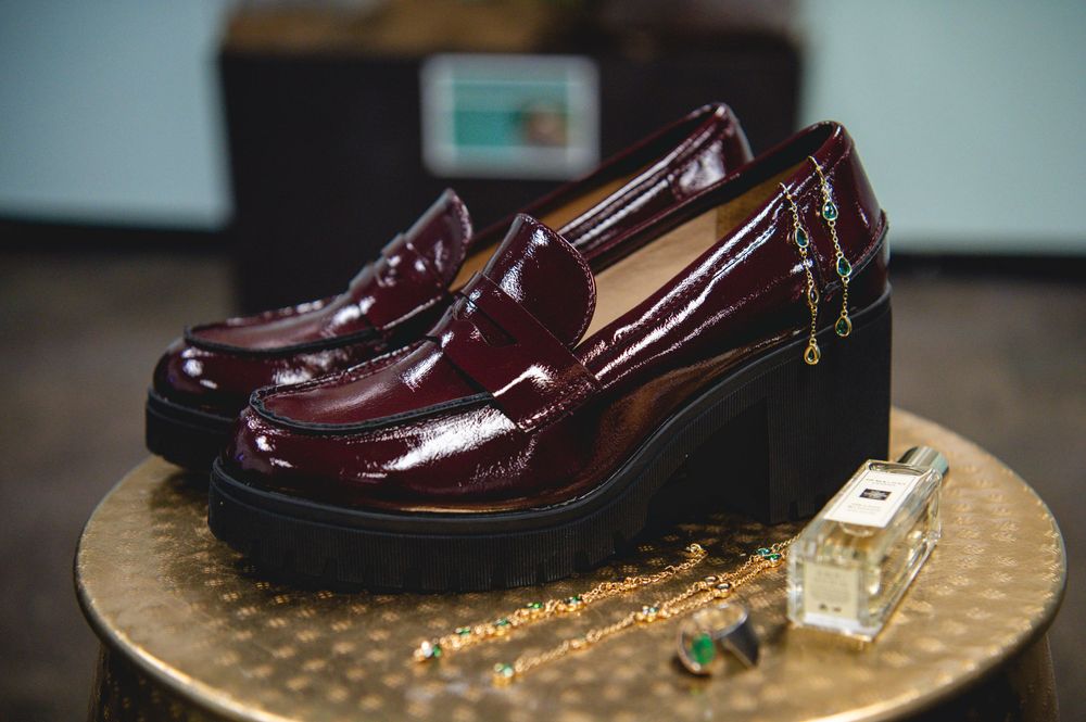 Burgundy patent leather platform loafers displayed on a gold tray with jewelry and perfume bottle.