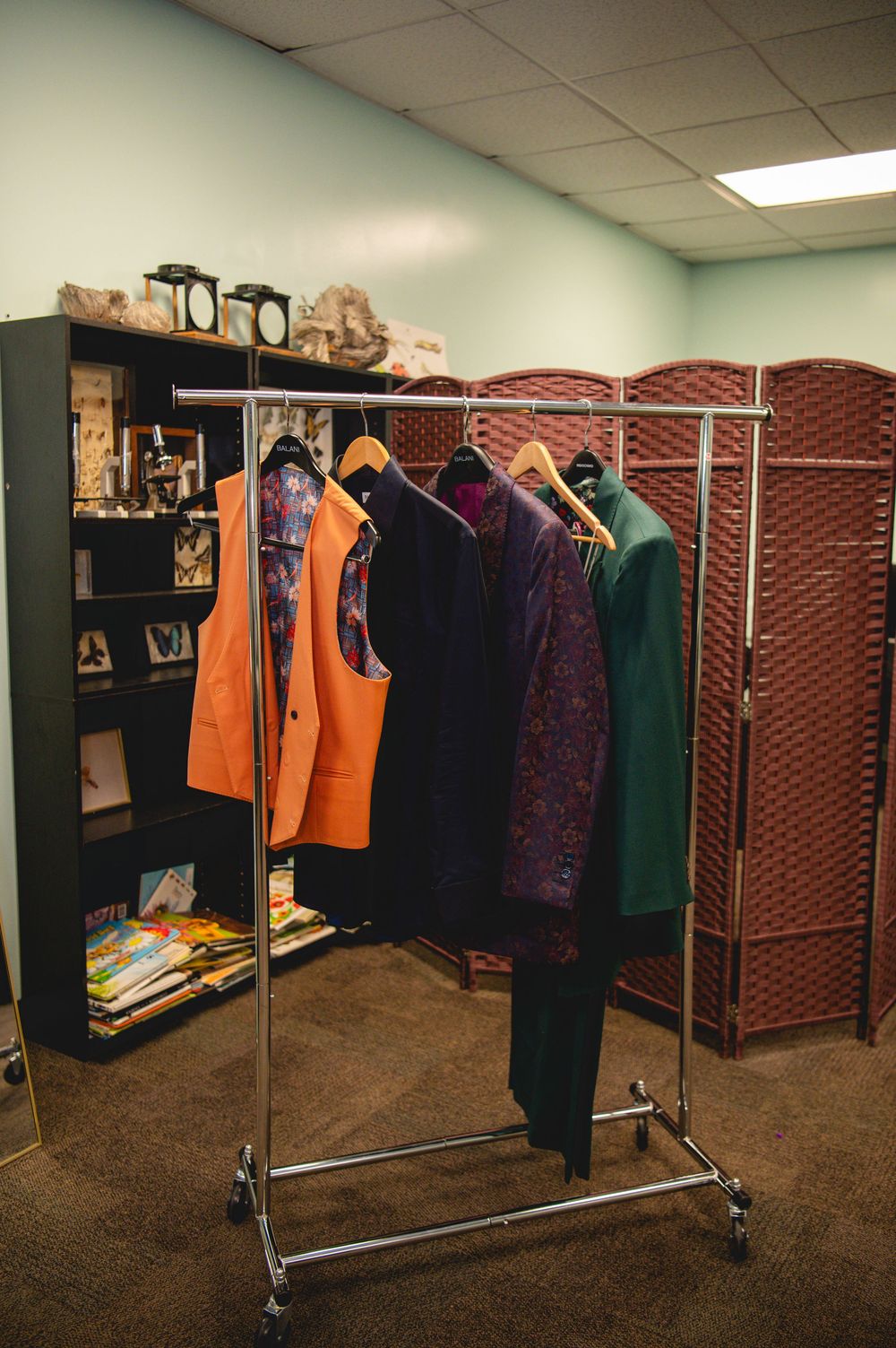 Clothing rack with colorful garments near a bookshelf and folding screen room divider in an office space.