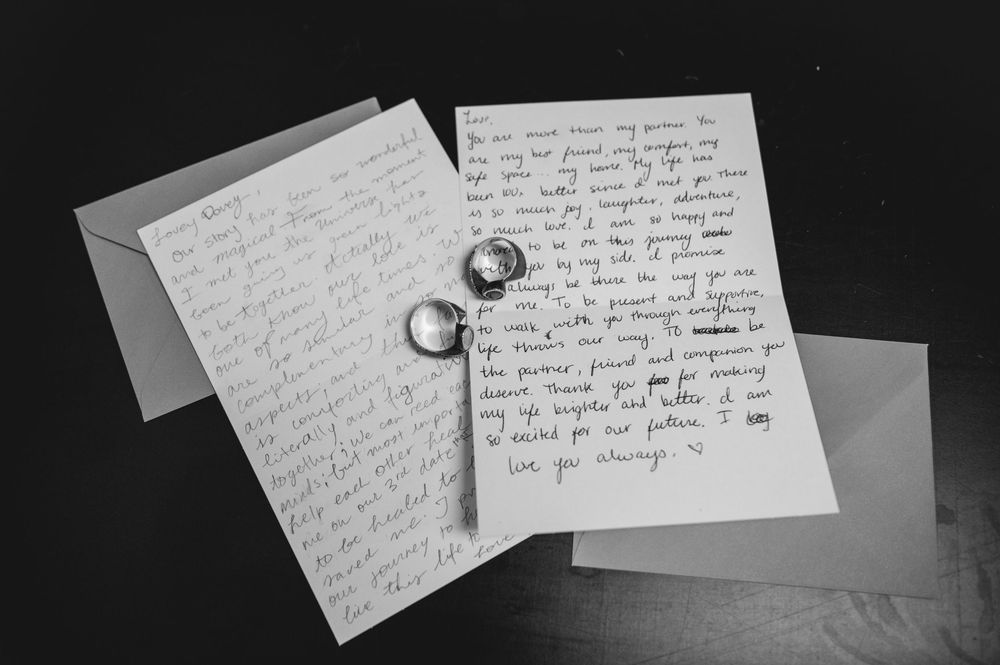 Black and white photo of handwritten wedding vows letters with two gold rings resting on top.
