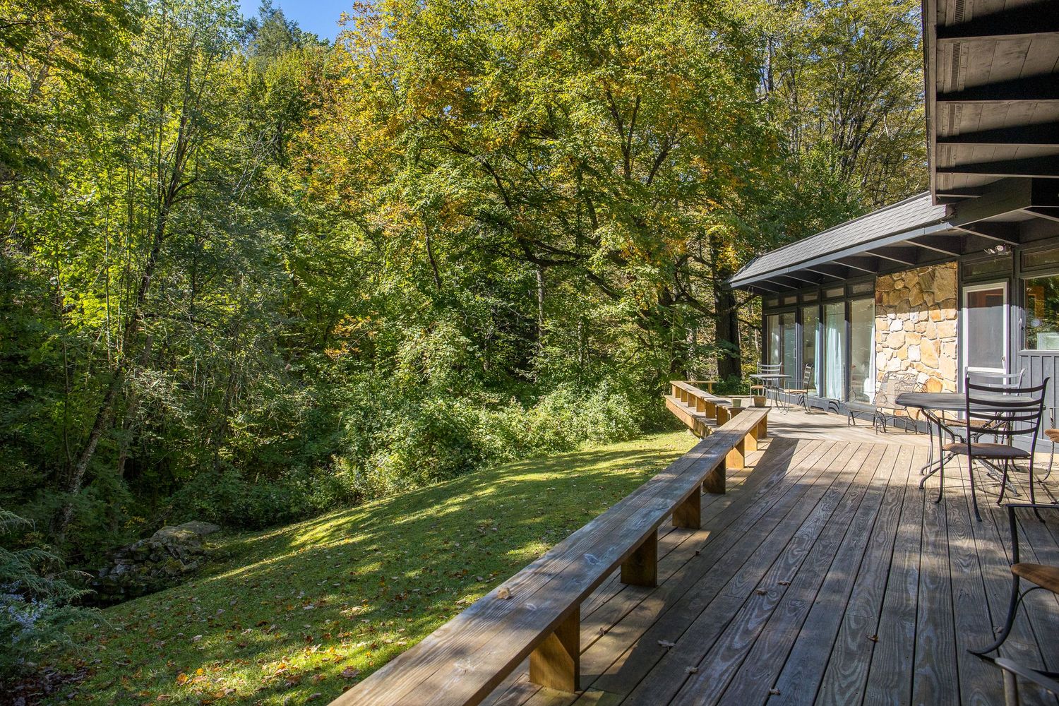 Spacious wooden deck overlooking a lush green forest with outdoor seating area.