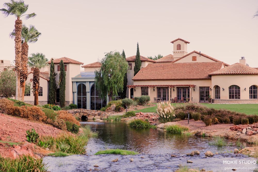 Elegant Spanish-style estate with terracotta roof, lush landscaping, and serene pond in a desert setting.