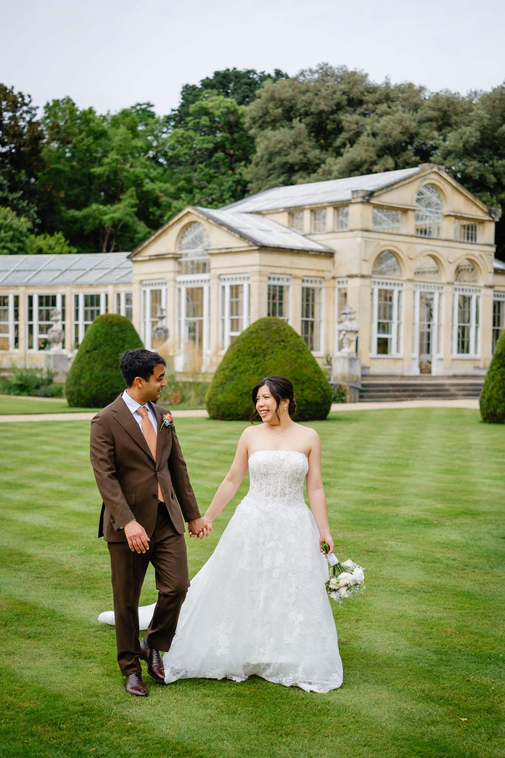bride and groom walking on the grass at the great conservatory in Syon park