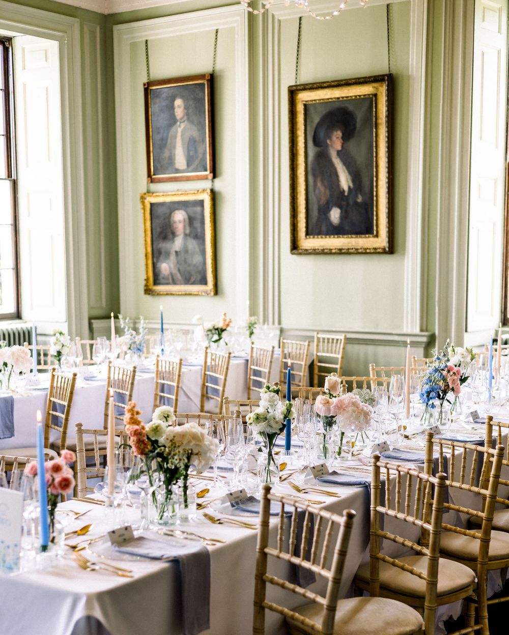 Elegant wedding reception in a green-walled room with gold Chiavari chairs, floral centerpieces, and classic portrait paintings.