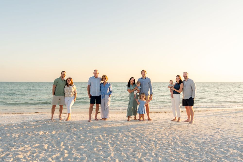 Extended family of eight adults and children posing together on white sand beach at sunset.