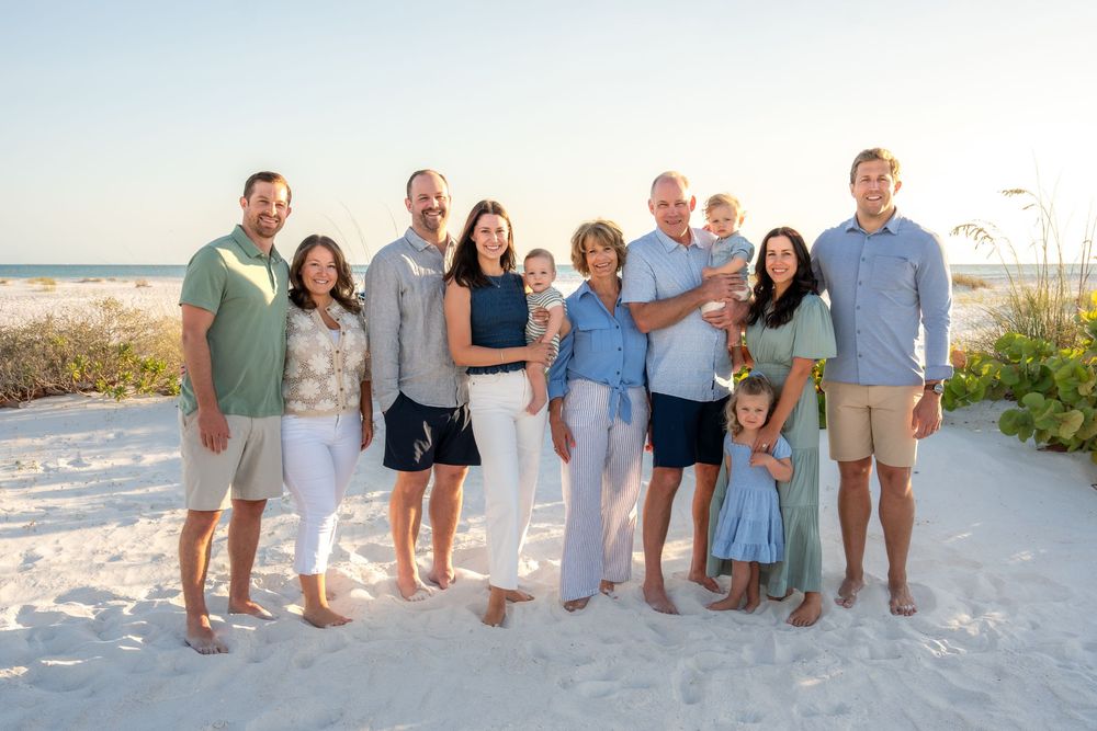 Large multigenerational family posing together on a sunny beach with sea oats in the background.