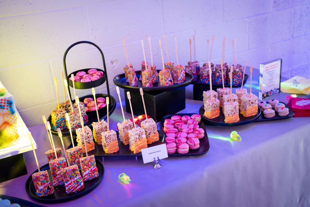 Colorful candy buffet table with cake pops, macarons, and decorated treats at a festive neon-themed party.