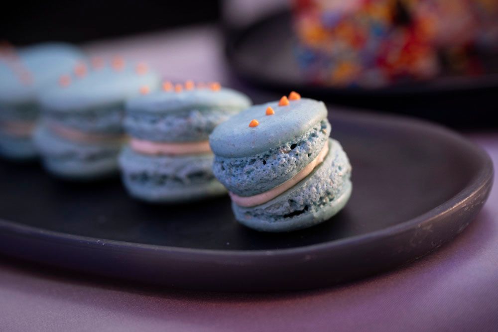 Blue macarons with orange sprinkles on a dark plate, showcasing elegant French pastry desserts.