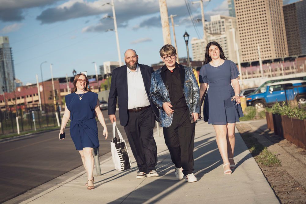 Four people walking together on a city sidewalk with a skyline in the background on a sunny day.