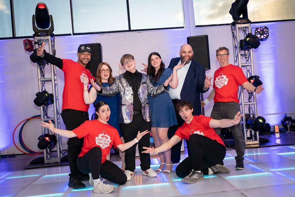 Group of eight people posing on a dance floor at an event, some wearing red t-shirts, under stage lighting.