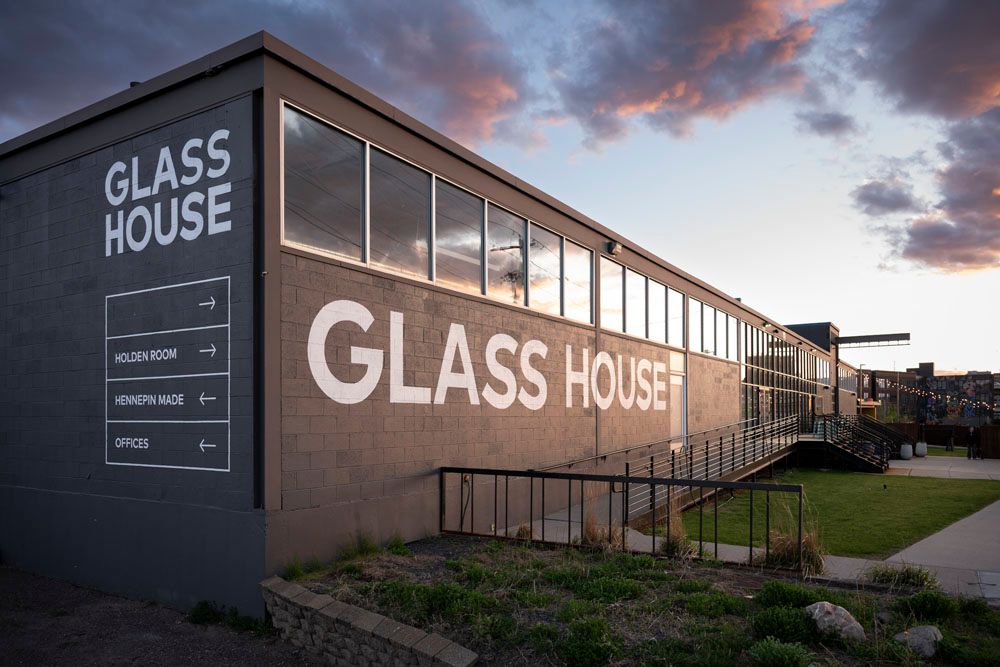 Exterior view of the Glass House building at dusk, featuring bold signage and large windows against a dramatic sky.
