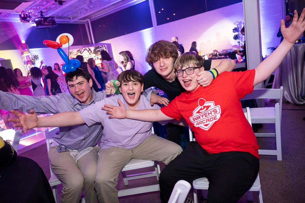 Four excited teenage boys pose energetically at a fun indoor celebration.