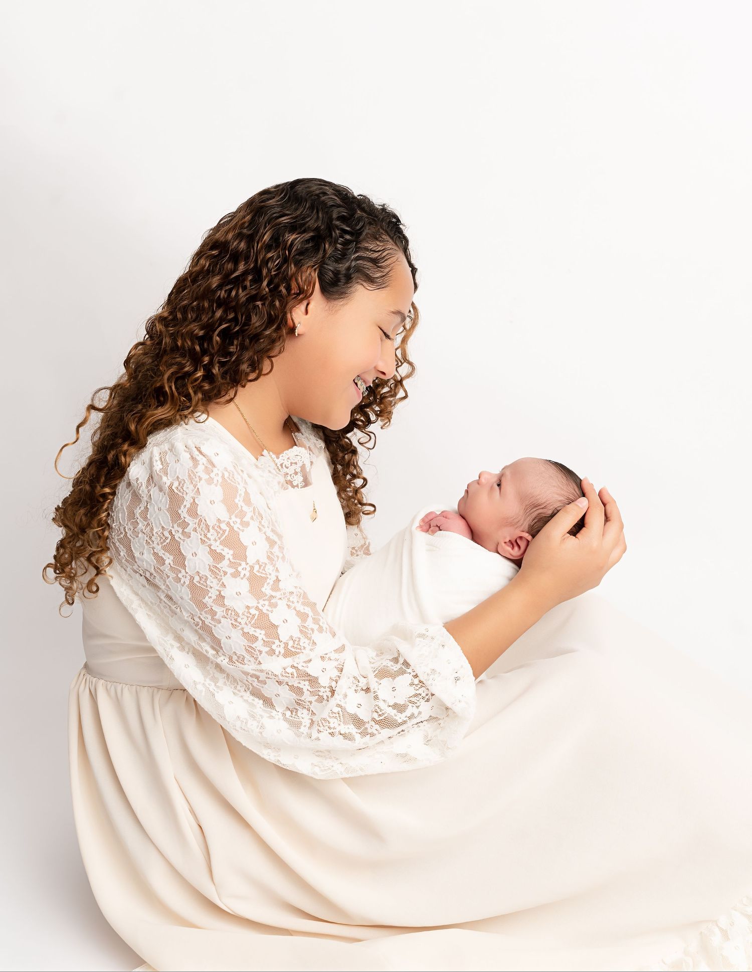 An older sister lovingly holds and looks at her newborn sibling during a studio newborn photography session in Zephyrhills, Florida.
