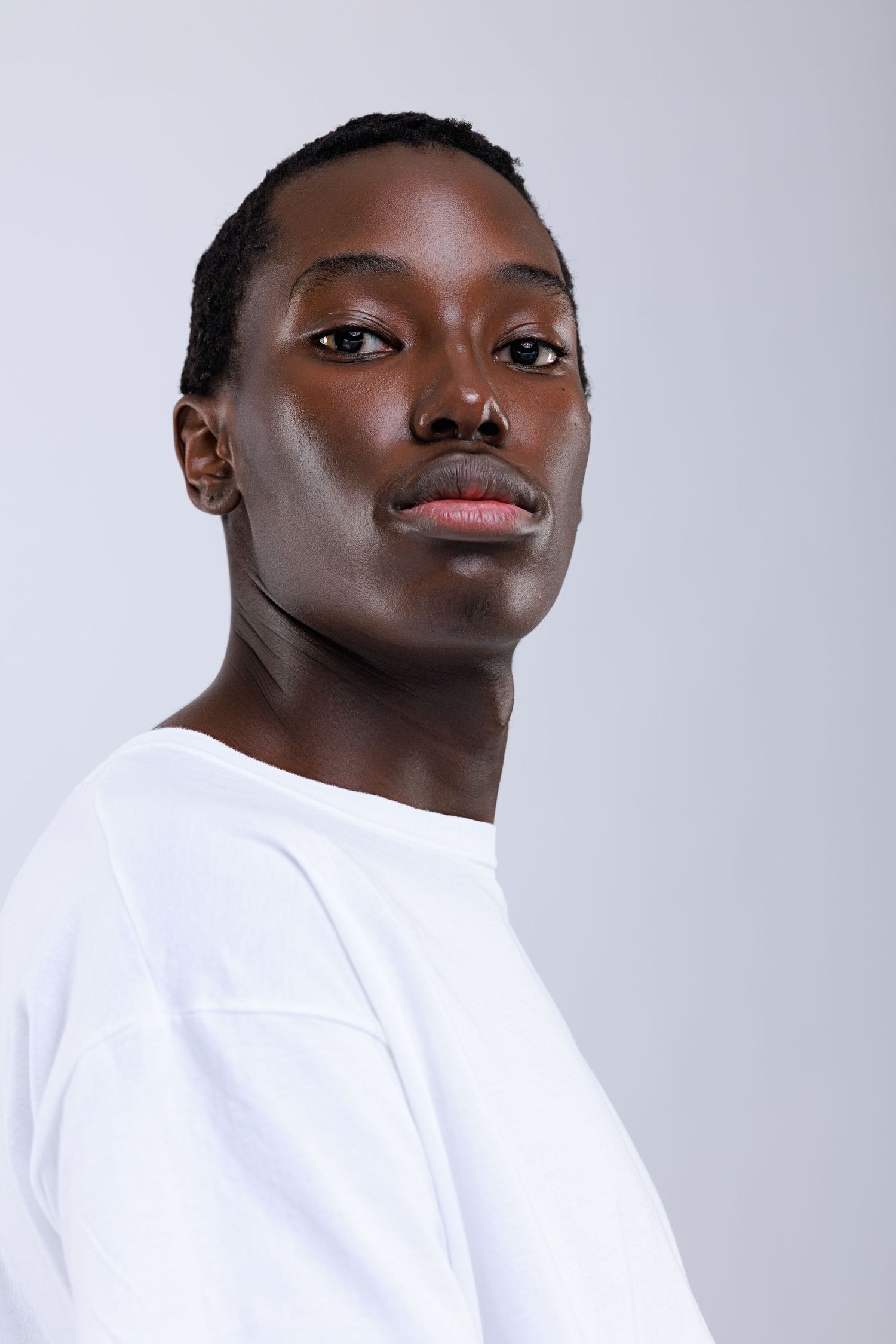 A young Black man in a white sweatshirt poses against a light gray background with a calm, confident expression.